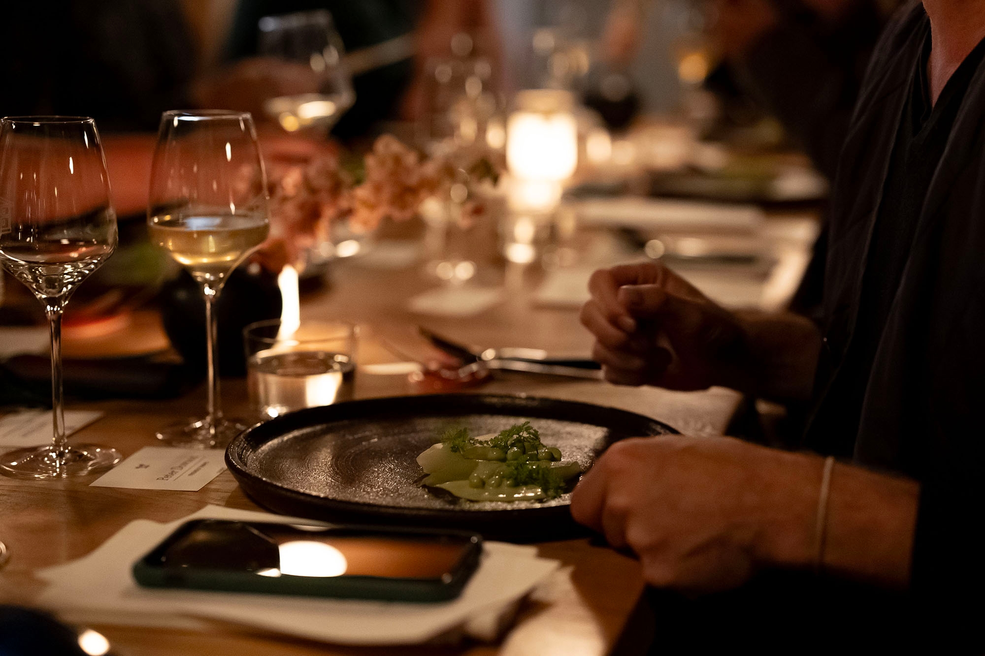 Table dressée pour un dîner gastronomique à l'Espace Old Mill, assiette en céramique noire avec plat du terroir, verres de vin blanc et bougies
