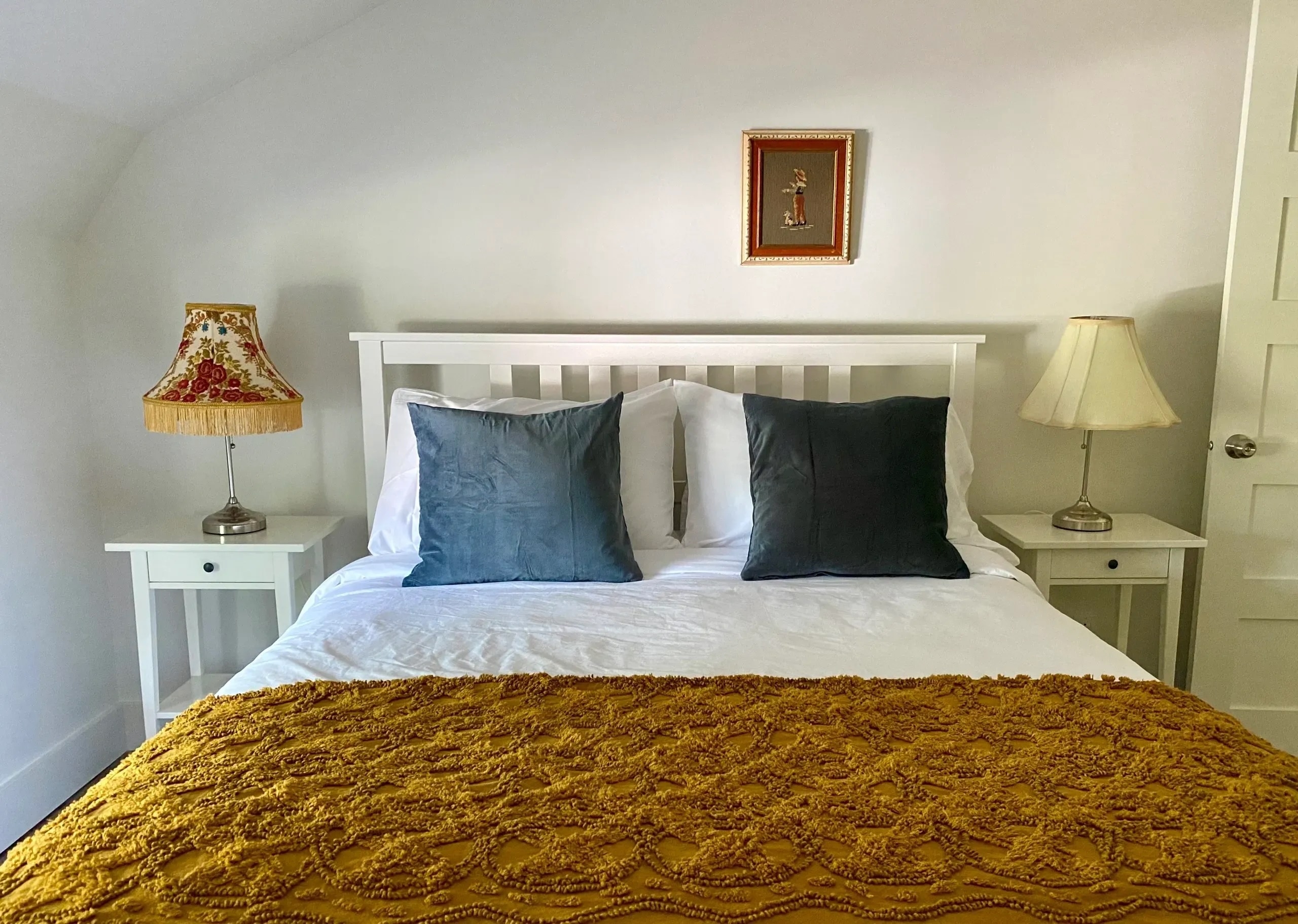 Chambre avec lit blanc, jeté jaune texturé et coussins bleus, lampes de chevet fleuries