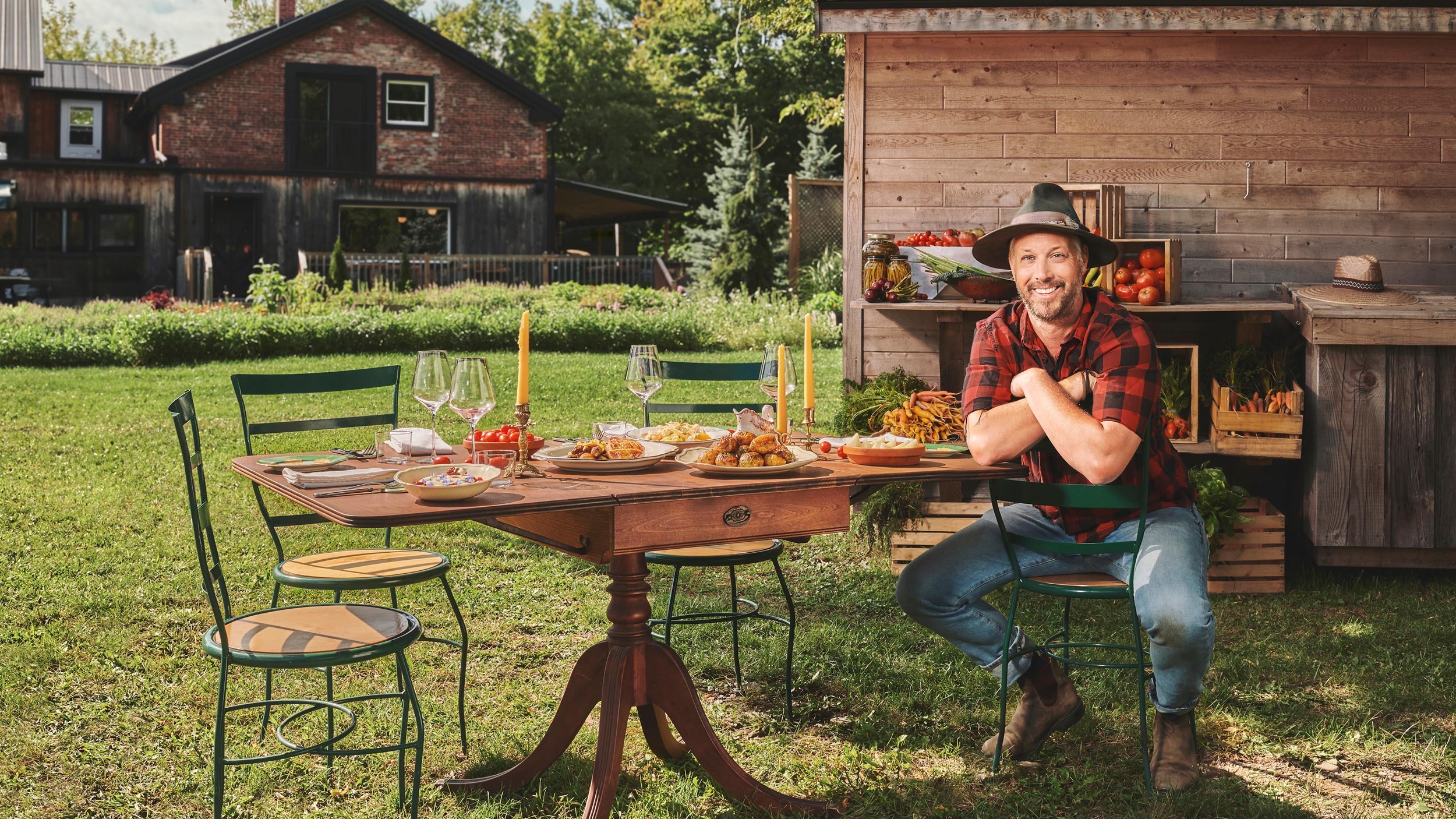 Jean-Martin Fortier attablé devant le Old Mill, entouré de récoltes du jardin, photo promotionnelle de la série La Table du Fermier